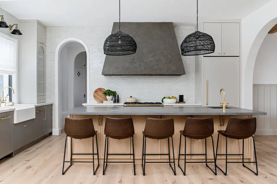 Concrete-look hood, black rattan pendants, brown leather stools and an arched doorway