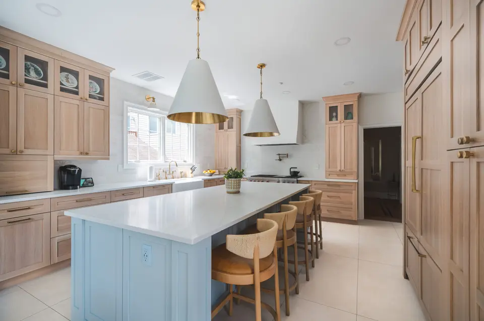 Light oak kitchen with a pale blue island, wood stools and white-and-brass pendants