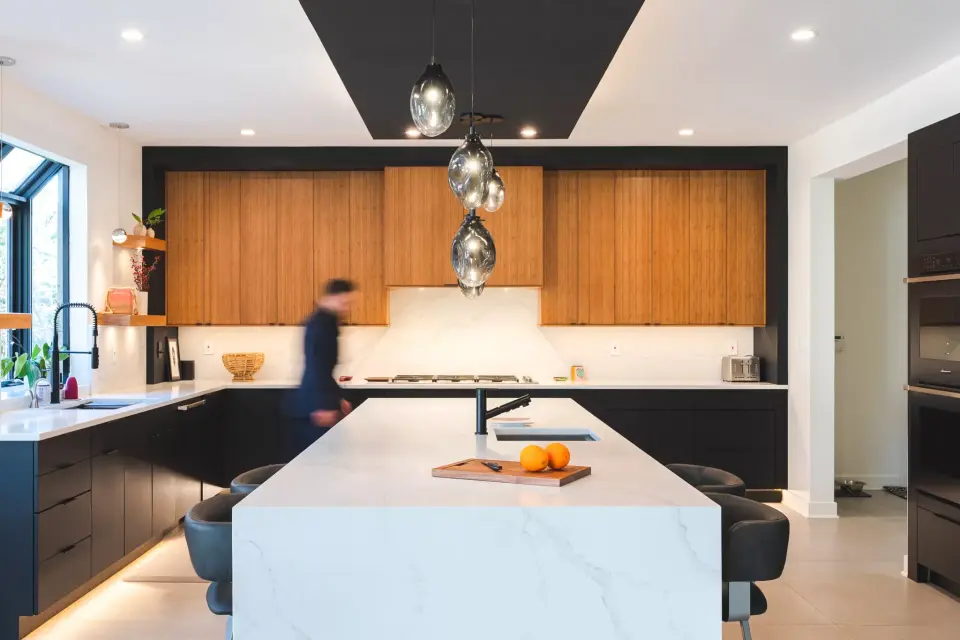 Walnut-veneer uppers, black lowers and a white waterfall island under a black dropped ceiling panel