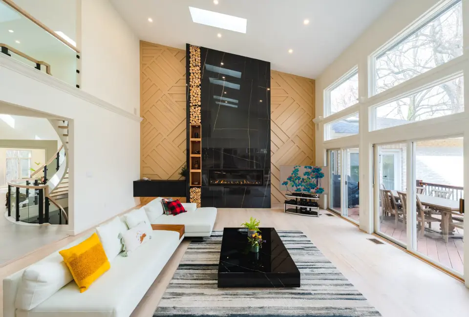 Double-height living room with a black stone fireplace wall, a stacked-log niche, white sofas and tall windows