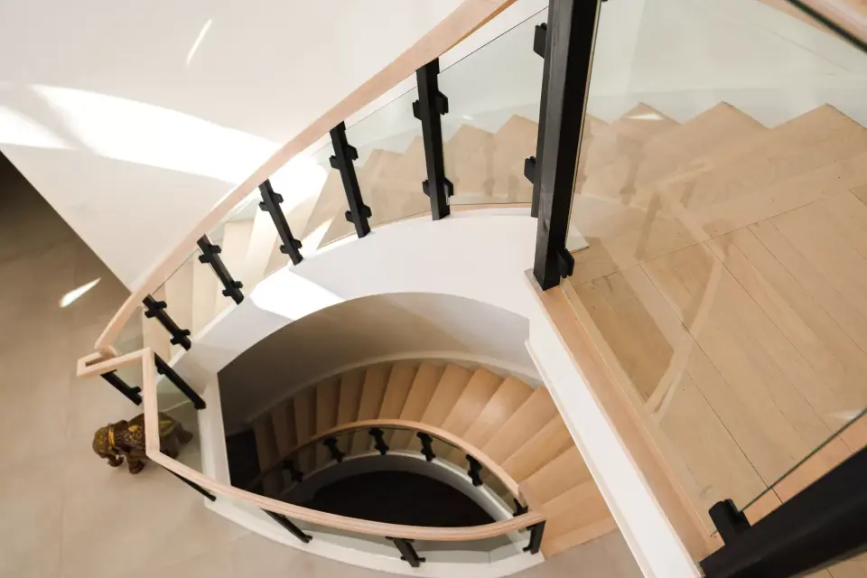 The curved staircase from above, glass rail and pale wood treads