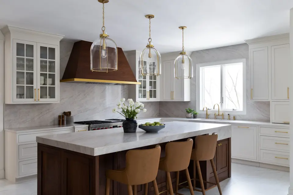 Walnut island with leather stools, stone counters, a copper-and-brass hood and glass bell pendants