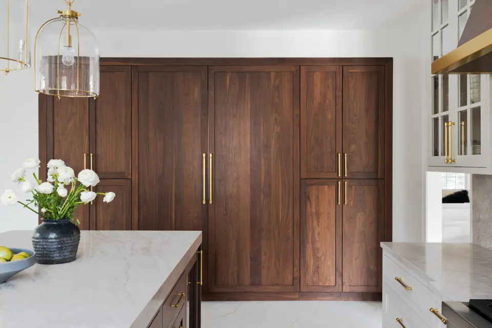 A wall of tall walnut cabinets with brass pulls, white flowers on the island