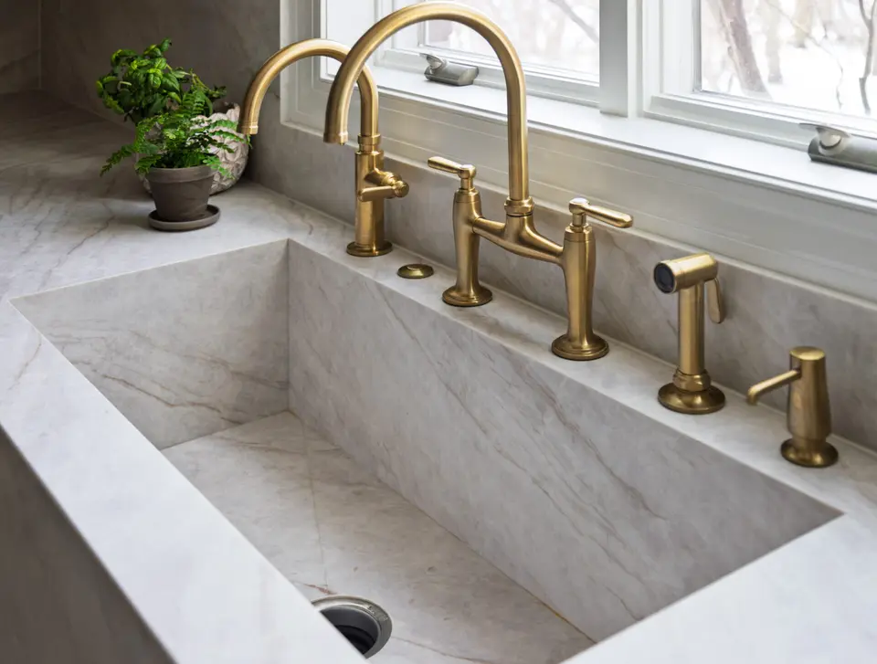 Brass bridge faucet over an integrated stone sink