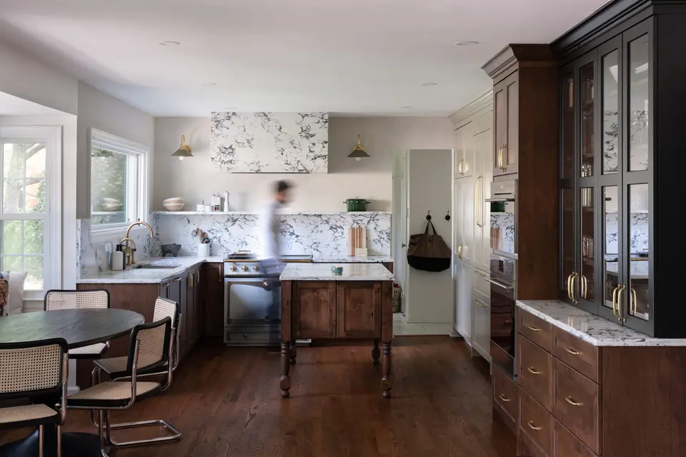 Walnut base cabinets, black glass-front cabinetry, a marble backsplash and hood surround, and a turned-leg wood island