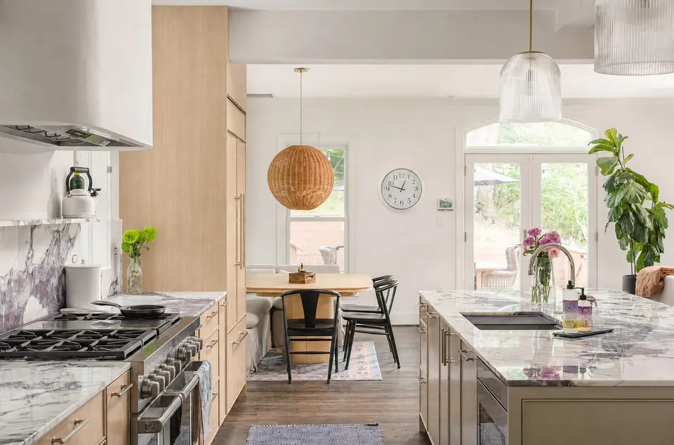 Light wood cabinets, marble counters and a gas range, with the island facing a dining nook