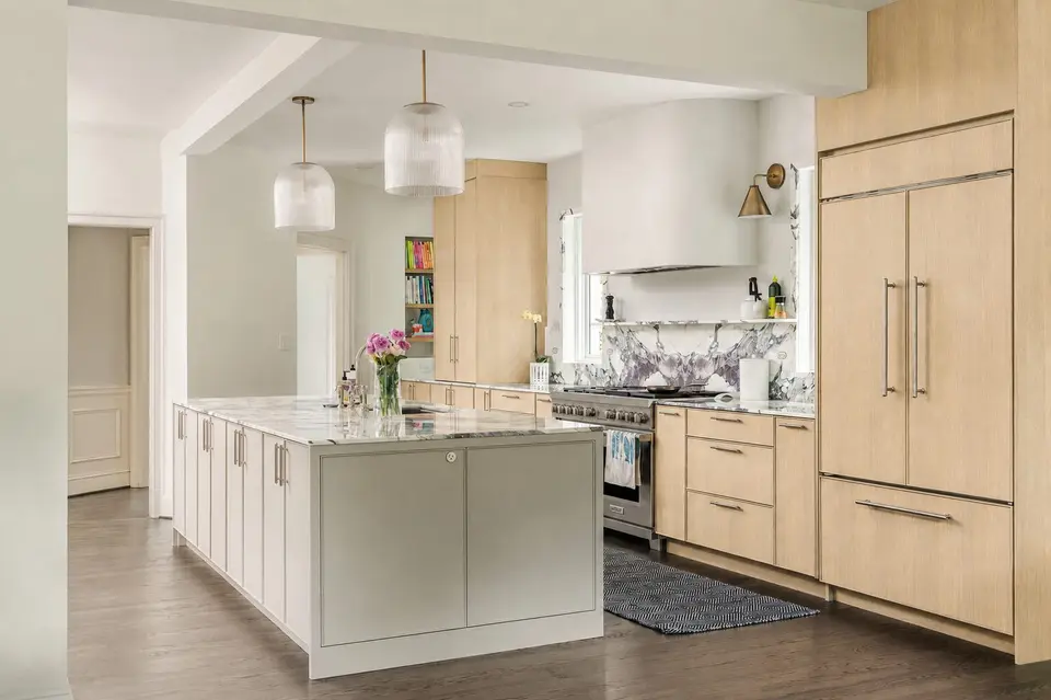 Wide view of the kitchen: pale grey island, white oak panelled refrigerator and plaster hood