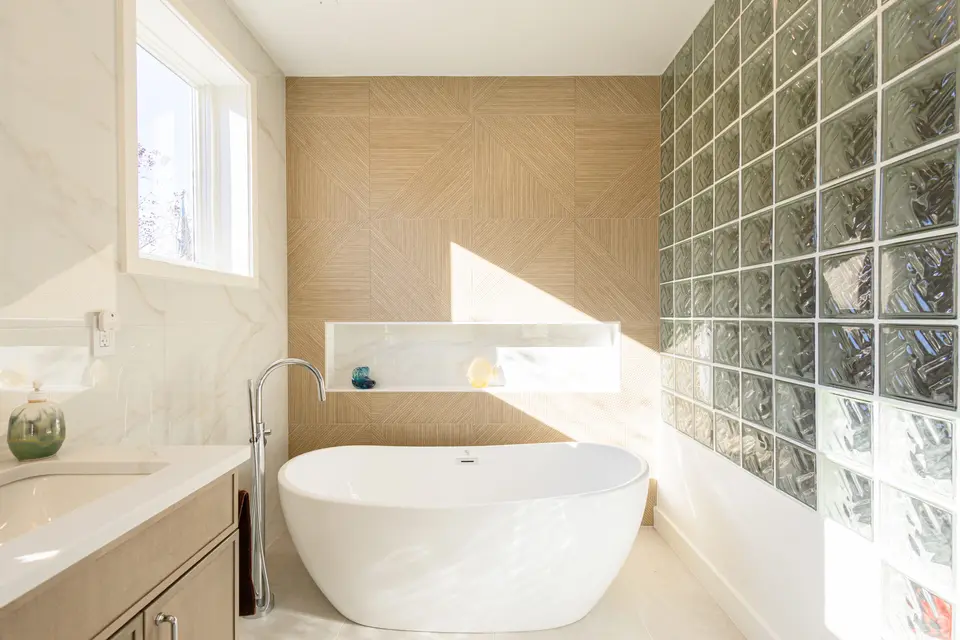Sunlit bathroom with a white soaking tub, a wood-grain herringbone wall and a glass-block wall