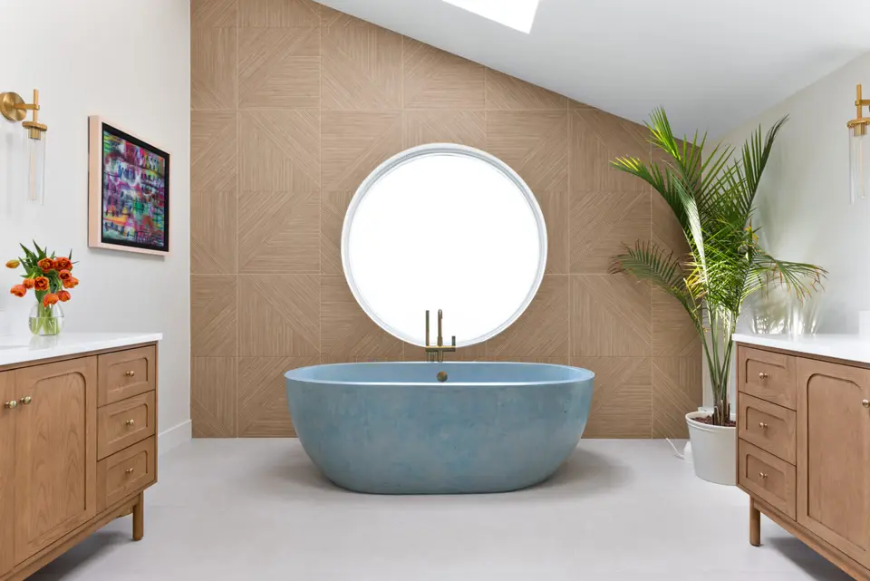 Blue stone soaking tub under a round window, a wood-tile feature wall, oak vanities and a palm