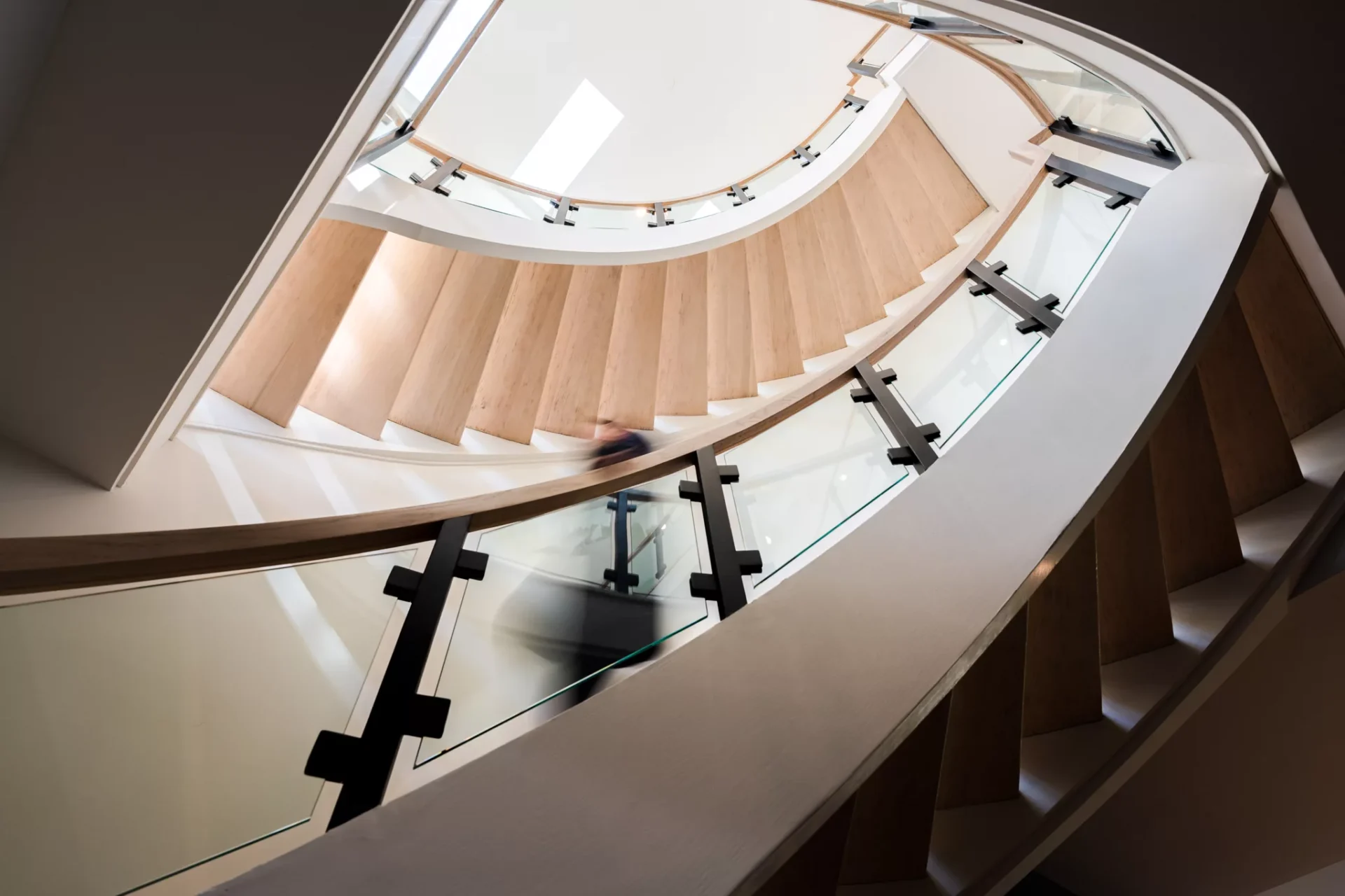 A curved open staircase with a glass rail, seen from above