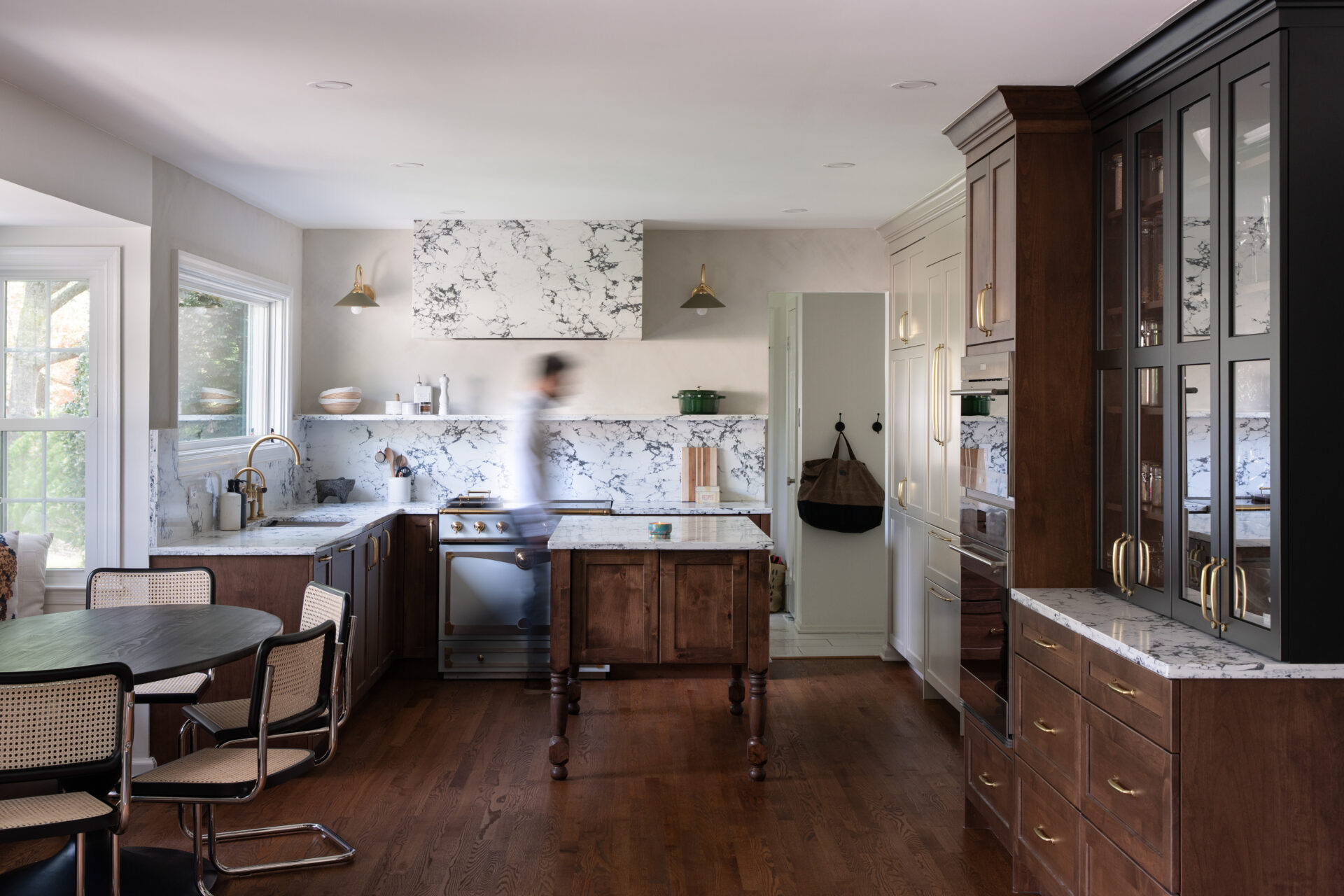 A kitchen with walnut base cabinets, black glass-front cabinetry, a marble backsplash and a turned-leg wood island