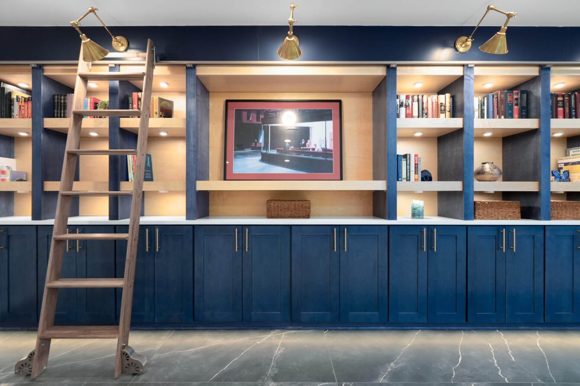 A navy built-in library wall with a rolling ladder and brass sconces